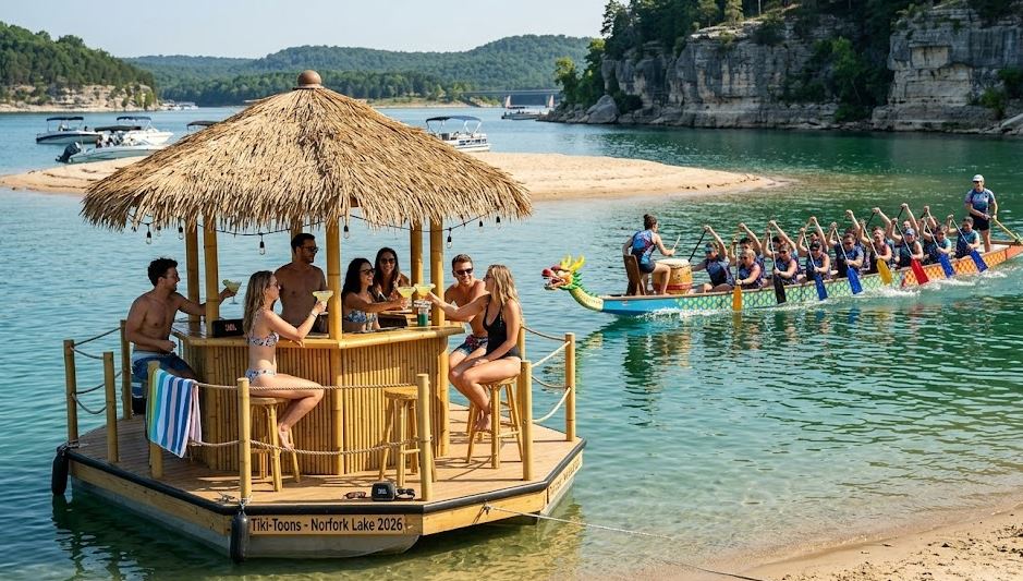 A group of diverse friends enjoys margaritas and laughter on a custom thatched-roof Tiki-toon boat named 'Tiki-Toons - Norfork Lake 2026', anchored near Sand Island on clear water, while a long, vibrant Dragon Boat with a drummer and active paddlers races through the lake, with the limestone bluffs of Robinson Point visible in the background and a distant 101 Bridge.