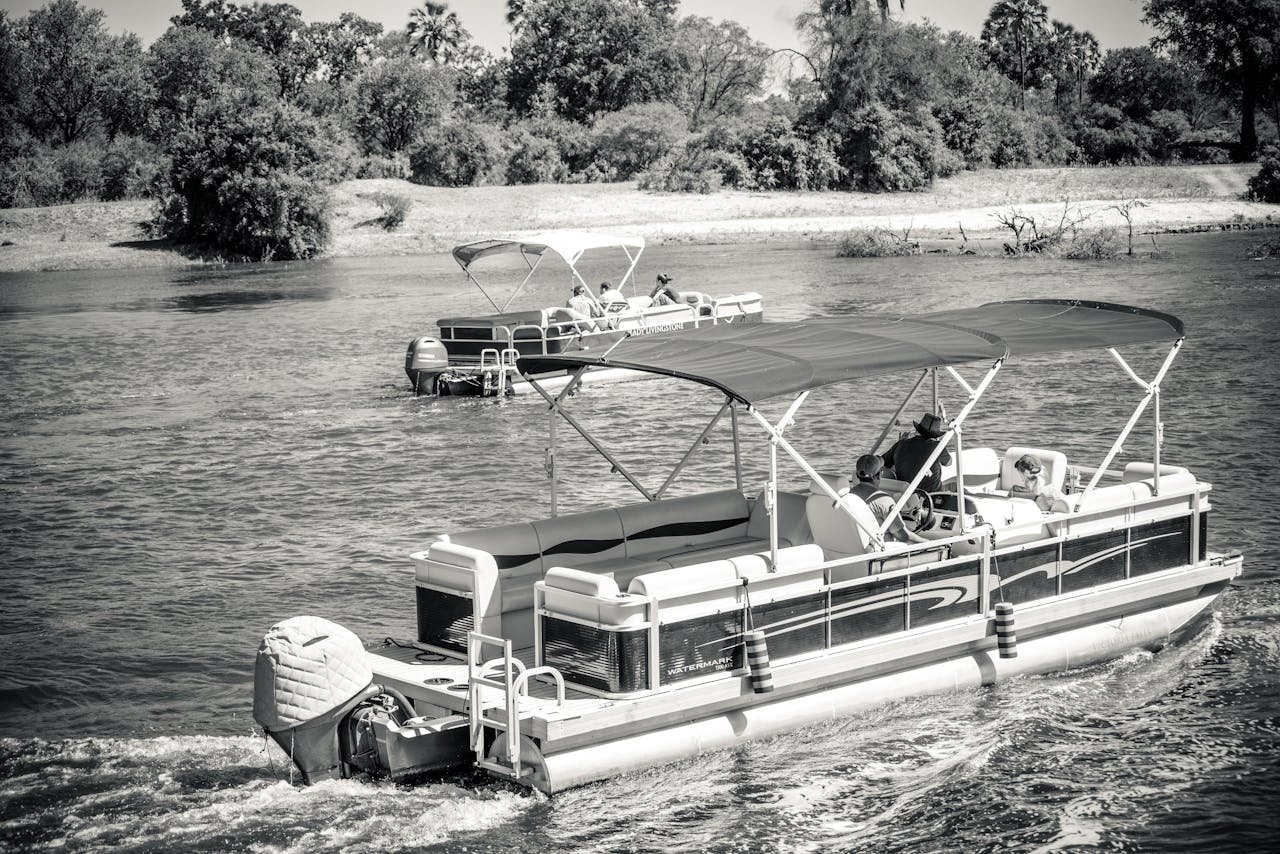 Pontoon boats cruising on a scenic river in monochrome, capturing leisurely travel and nature's beauty.