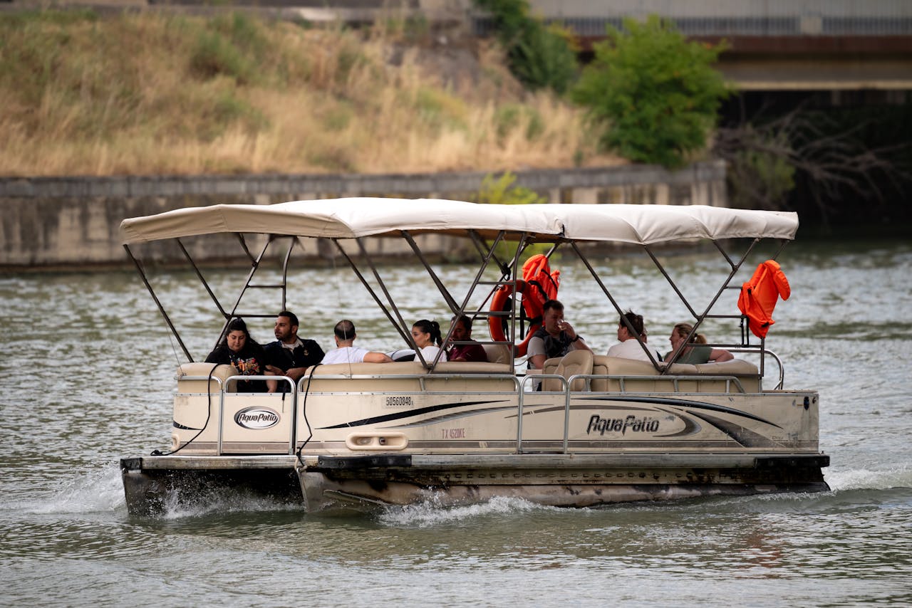 about-04 Pontoon boat cruising on a river with diverse passengers enjoying a sunny day in Tbilisi.